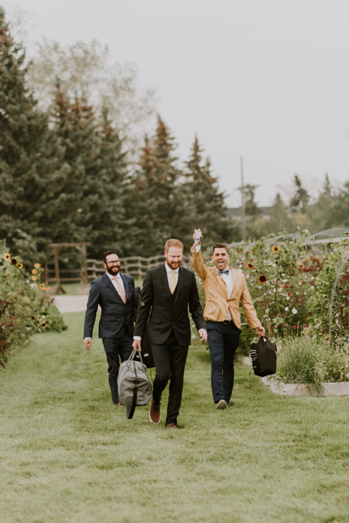 A group of groomsmen walking through a garden with luggage.
