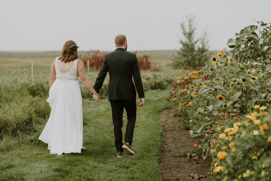 A bride and groom walk through a field of sunflowers.