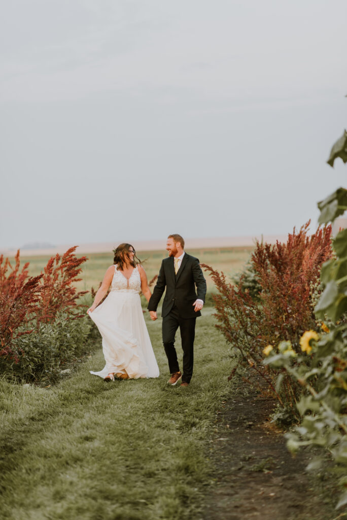 A bride and groom walking through a field of sunflowers.