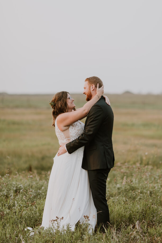 A bride and groom embrace in the middle of a field.