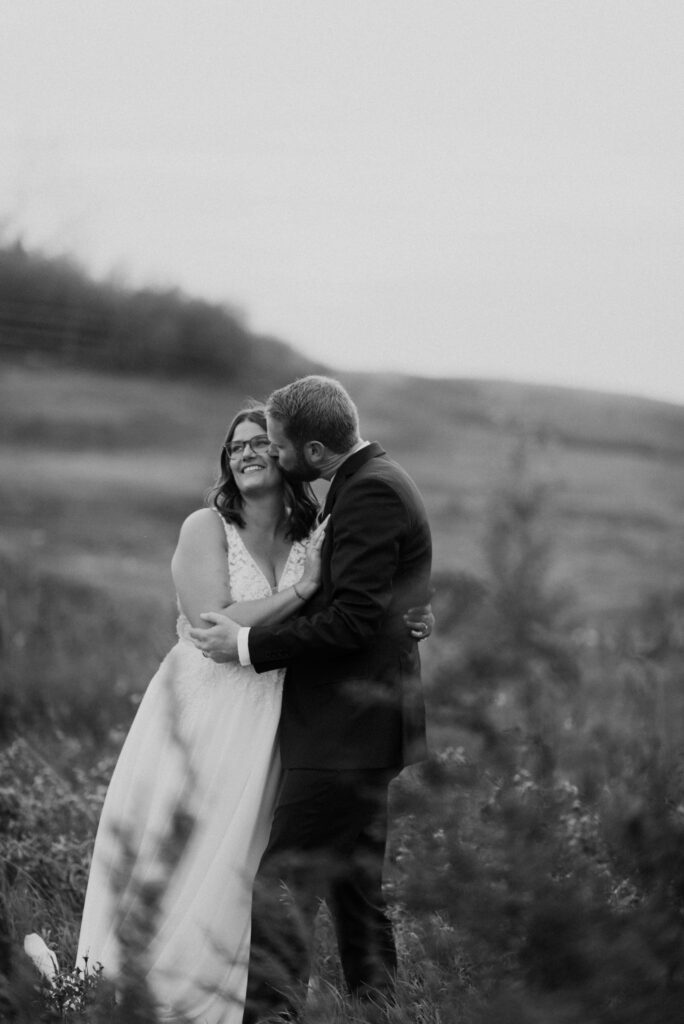 A bride and groom hugging in a field.