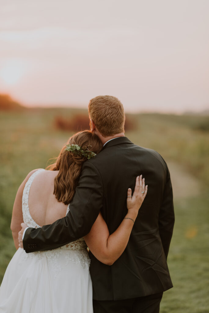 A bride and groom hugging at sunset in a field.
