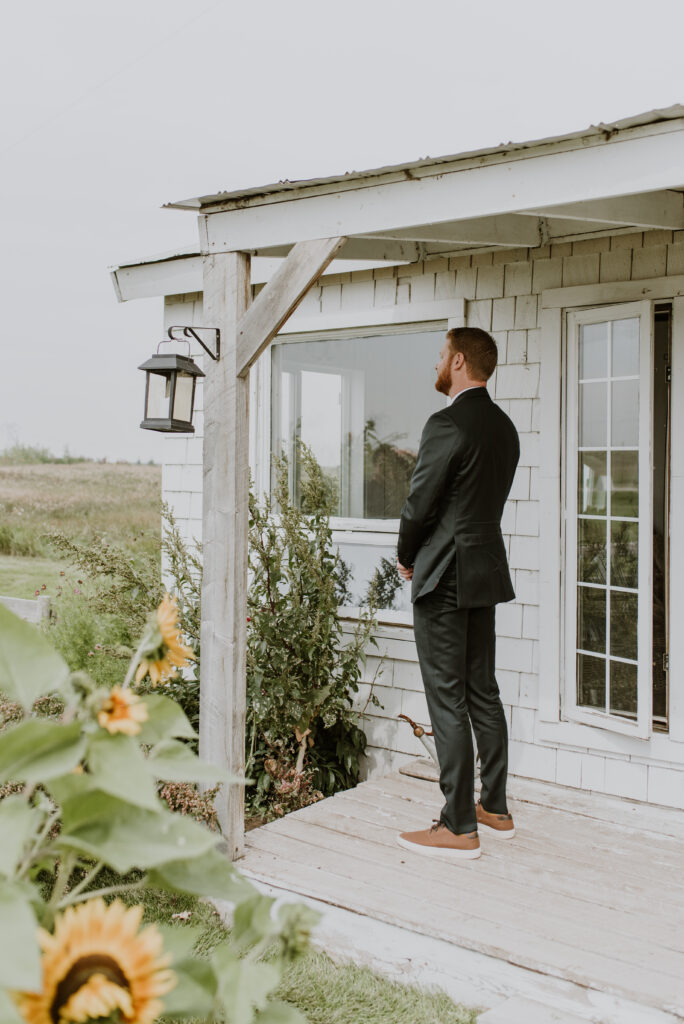 A man in a suit standing on the porch of the cottage awaiting his bride and their "First Look" on their wedding day. 