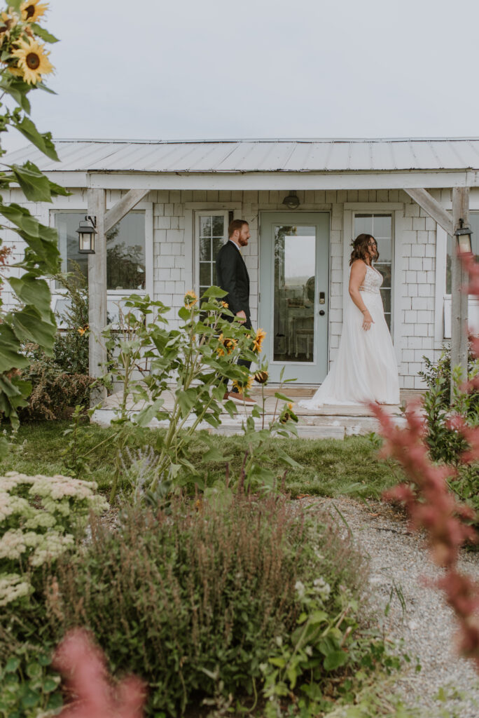 A bride and groom standing in front of the Gathered cottage with sunflowers.