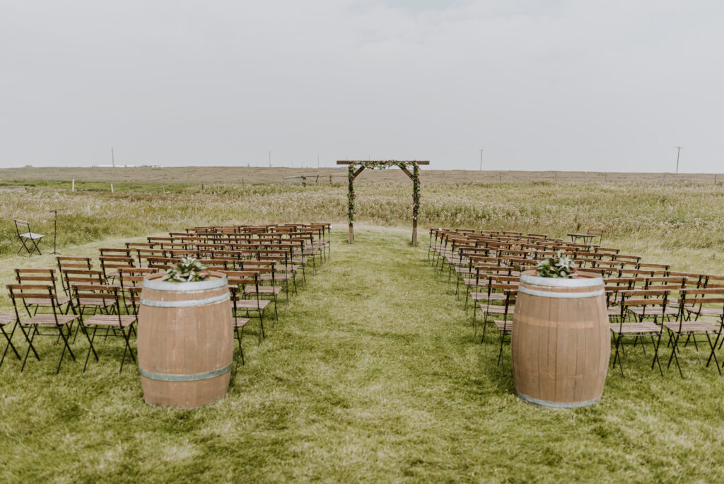 A wedding ceremony set up in a field with wooden barrels.