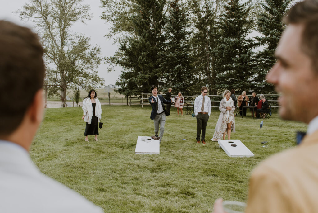 A group of people playing cornhole at an outdoor wedding.