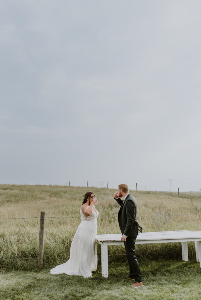 A bride and groom standing on a bench in a field.