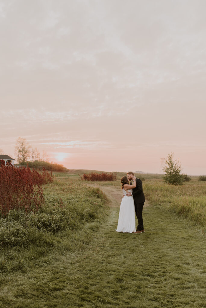 A bride and groom kissing in a field at sunset.