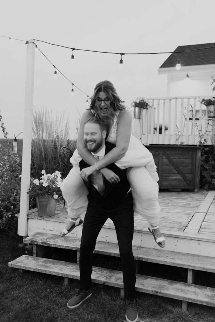 Black and white photo of a bride and groom riding each other on a wooden deck.