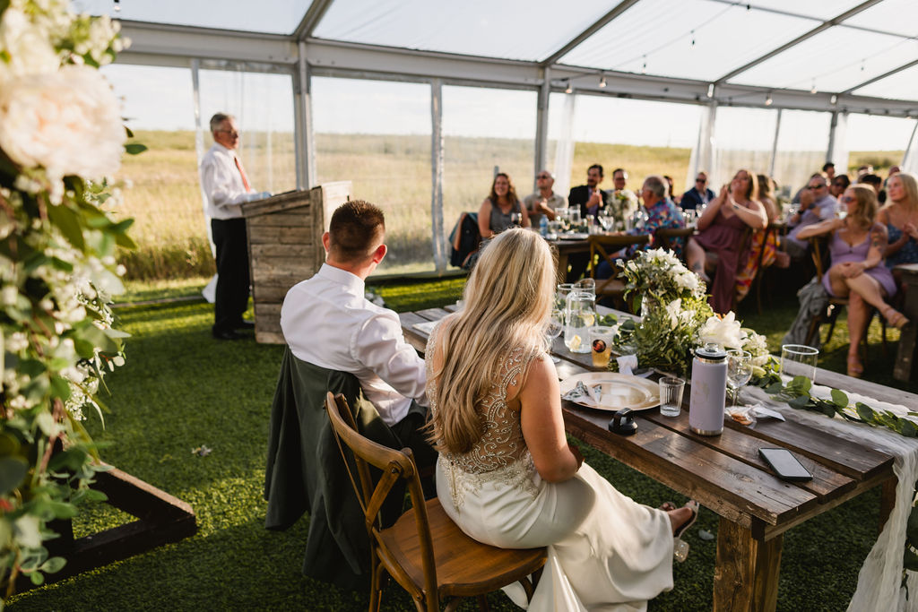 A wedding reception in a tent with people sitting at tables.