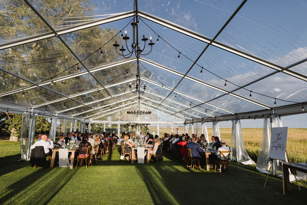 A clear tent with tables and chairs in the middle of a field.