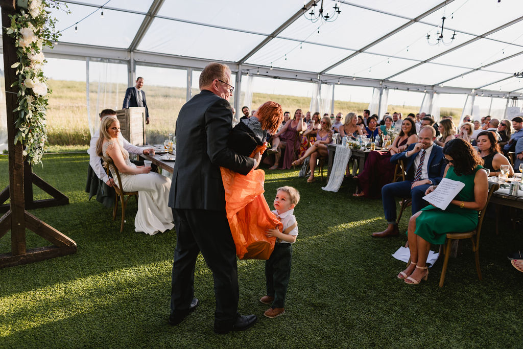 A man is holding a child during a wedding ceremony in a tent.