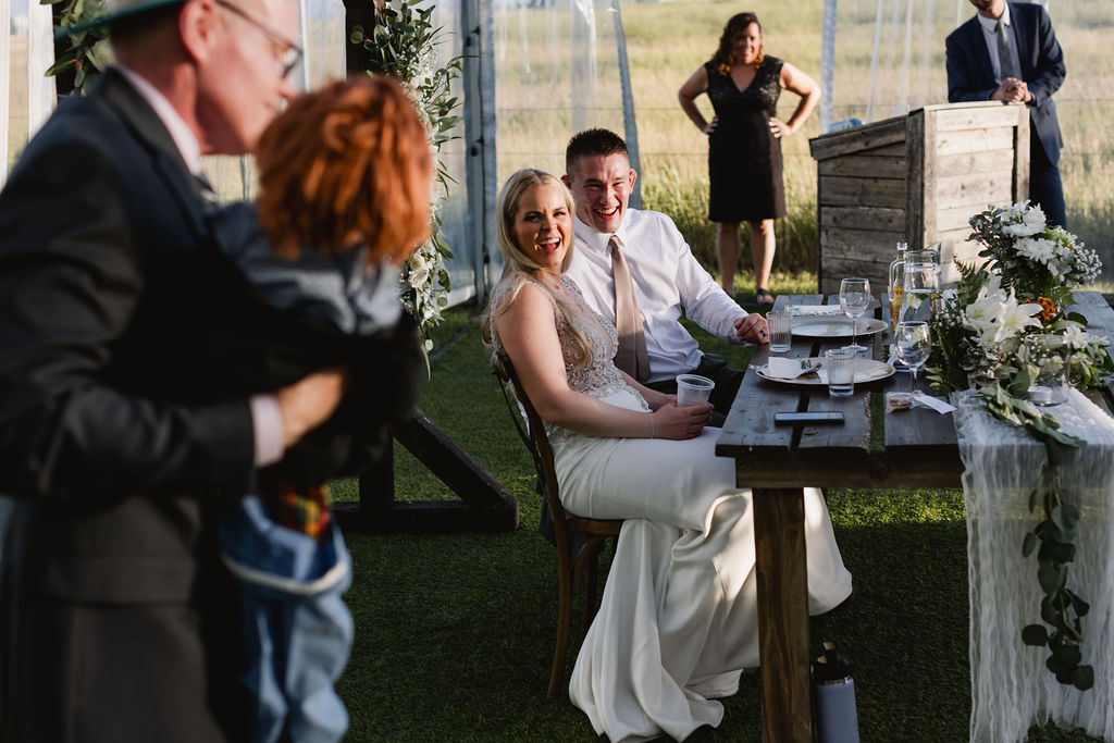 A bride and groom sitting at a table in a field.