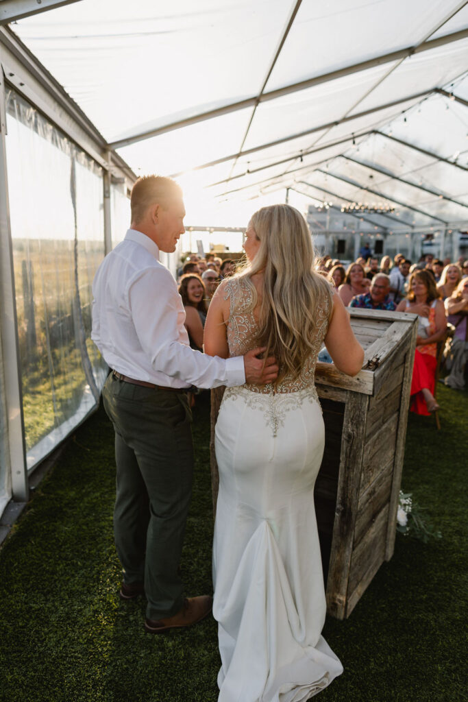 A bride and groom stand in front of a tent during their wedding ceremony.