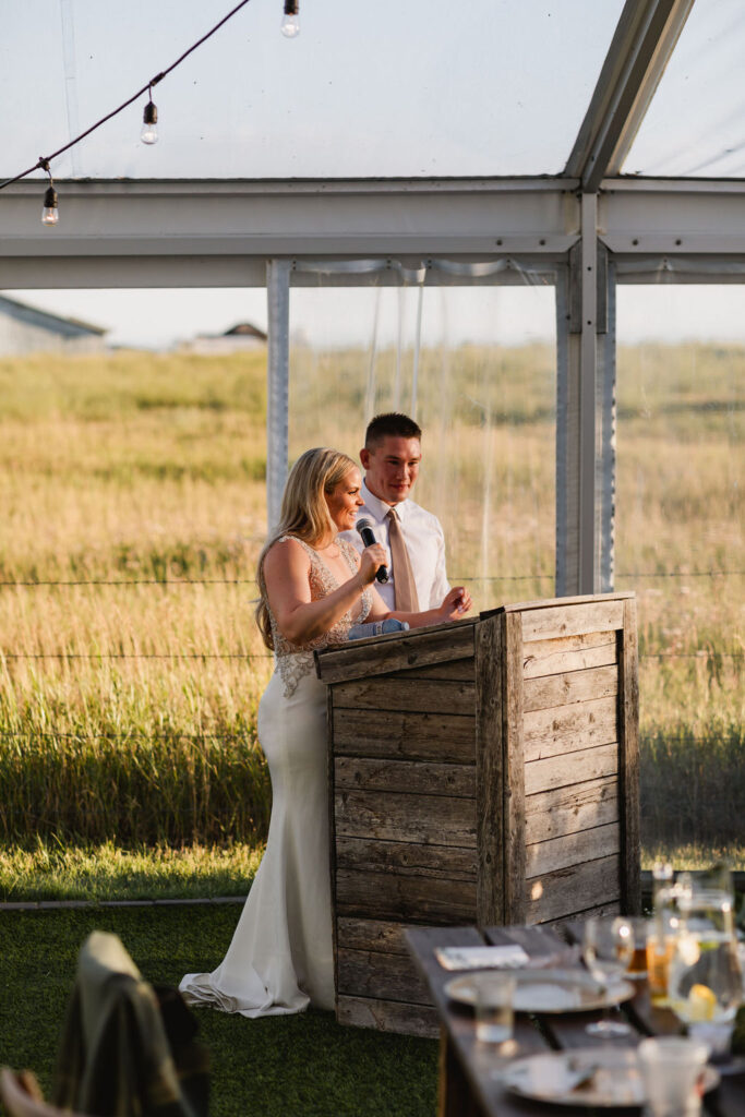 A bride and groom giving a speech in a tent.
