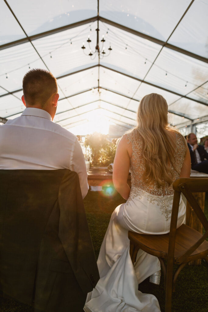 A bride and groom sitting at a table in a tent.