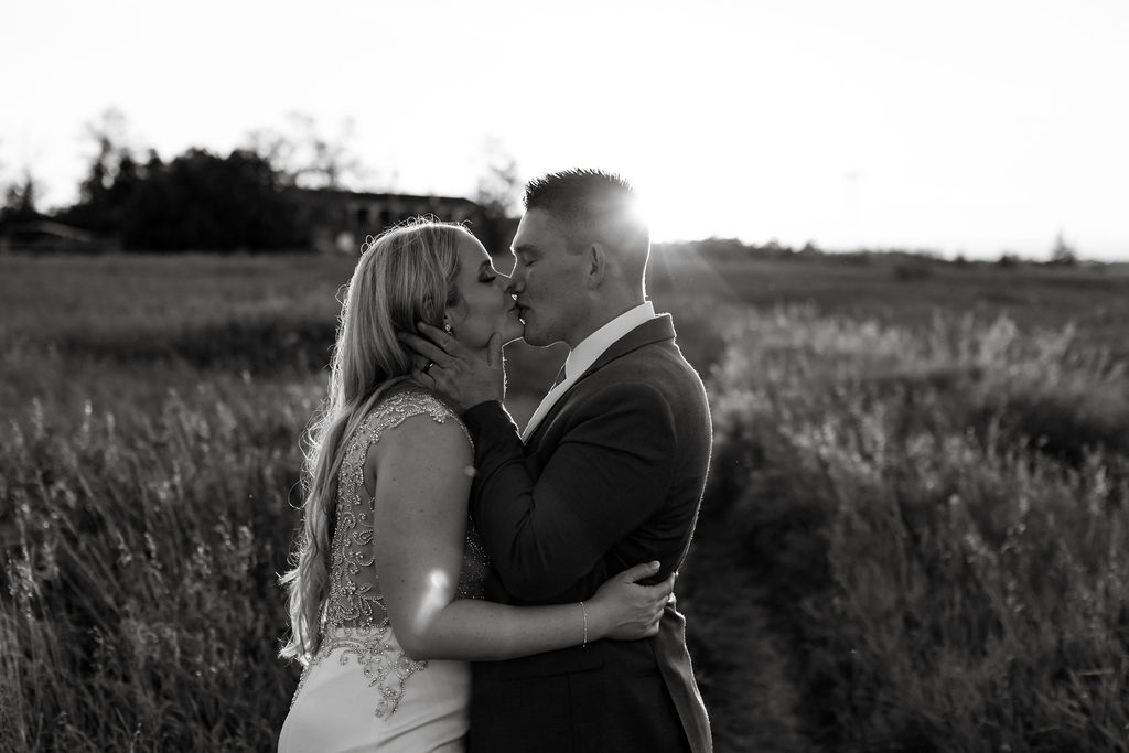 A bride and groom kissing in a field at sunset.