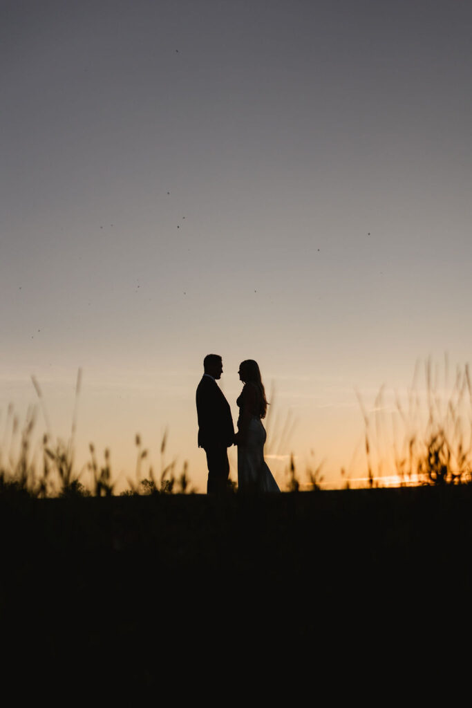A bride and groom silhouetted at sunset in a field.