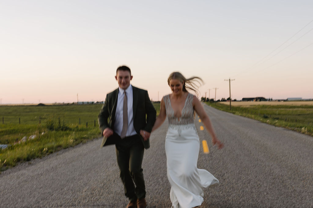 A bride and groom walking down a road at sunset.