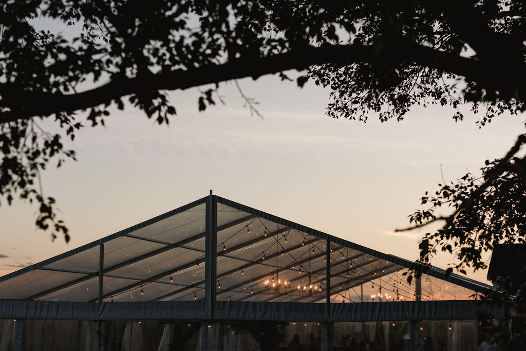 A wedding tent at sunset with trees in the background.