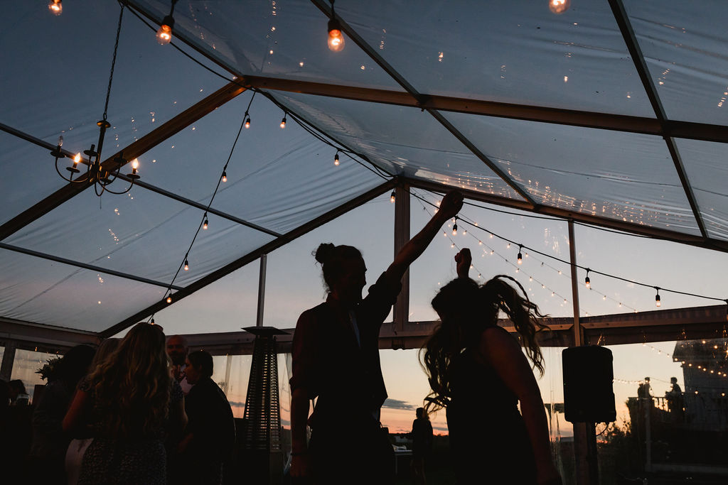 A group of people dancing in a tent at sunset.
