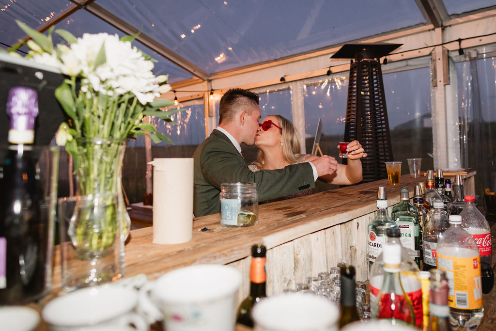 A bride and groom kissing in front of a bar.