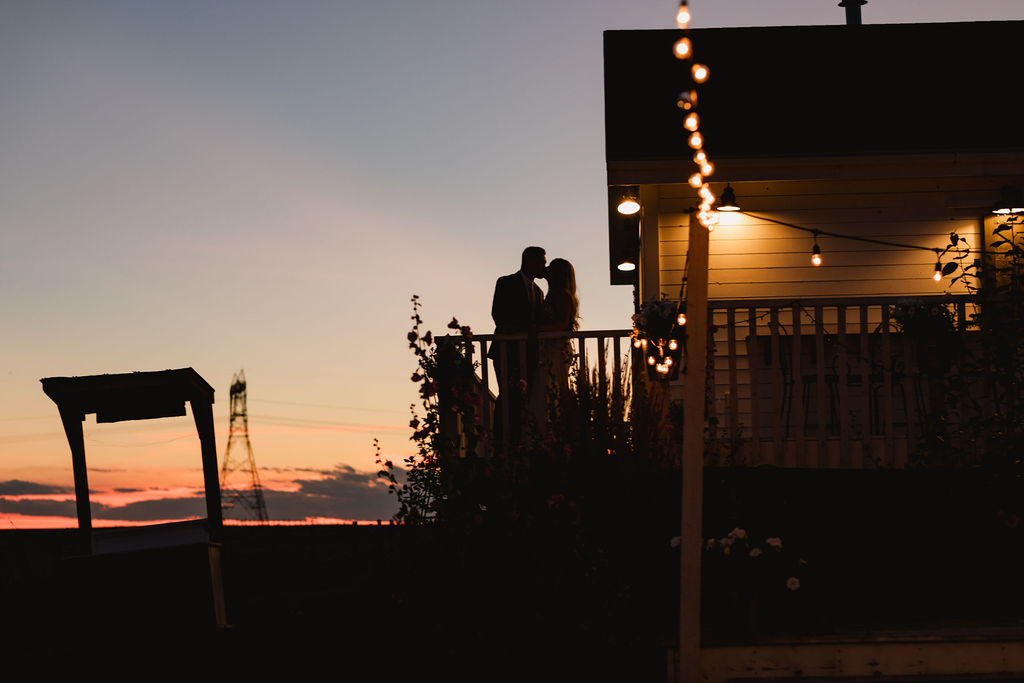 A couple standing on the porch of a house at sunset.