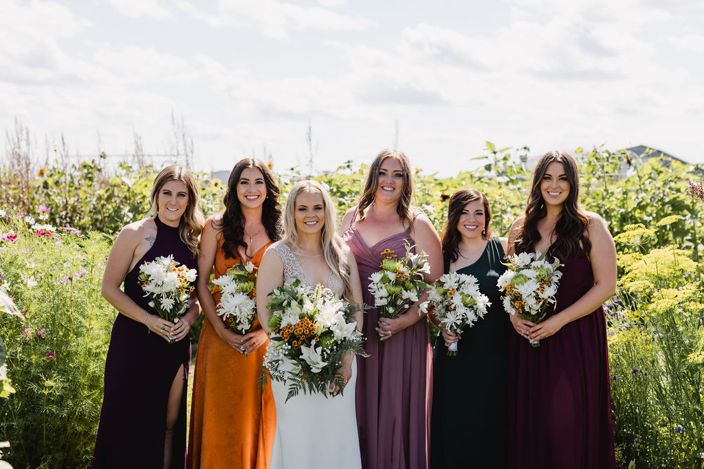 A group of bridesmaids in colorful dresses in a field. In mix matched  dresses holding DIY wedding floral bouquets