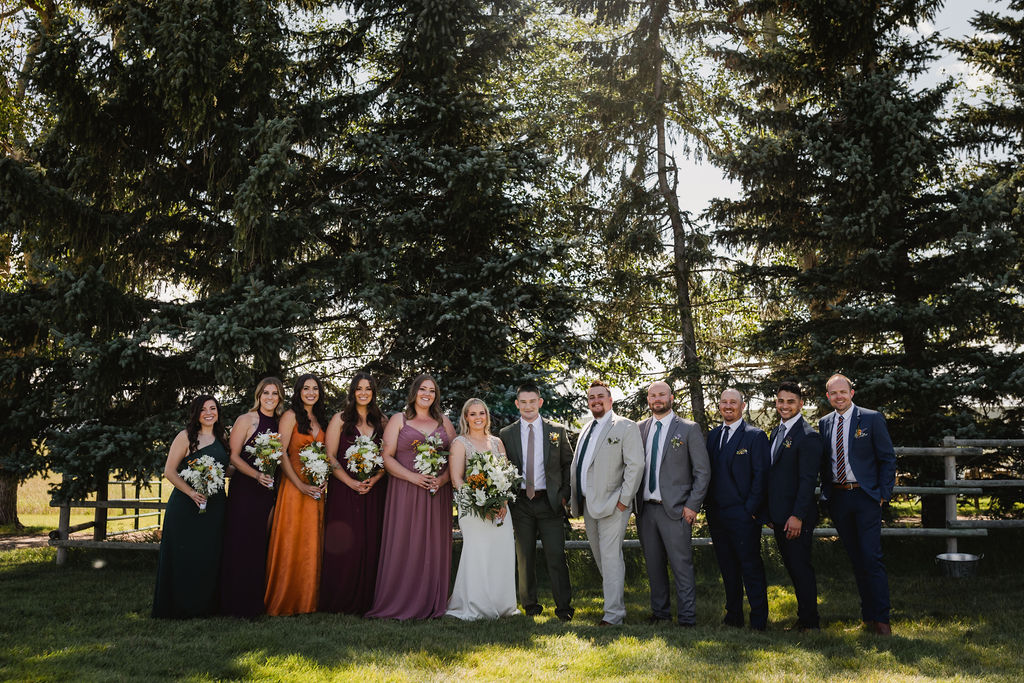 A group of bridesmaids and groomsmen posing in front of a tree.