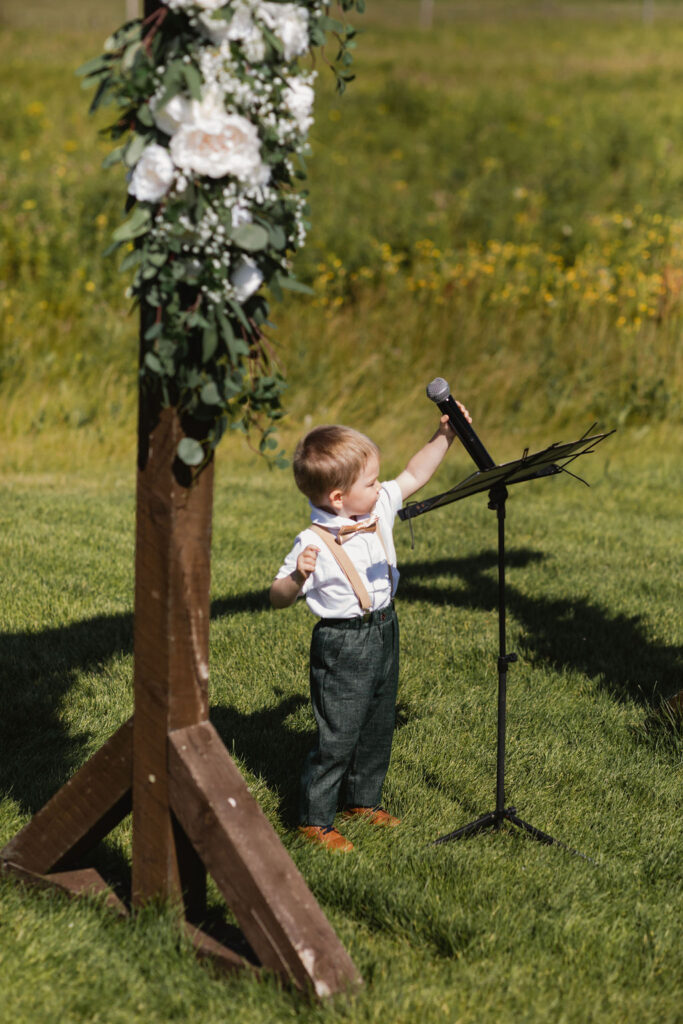 A boy standing in a grass field holding a microphone.