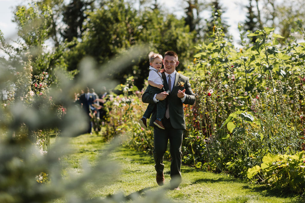 A man carrying a child through a garden.