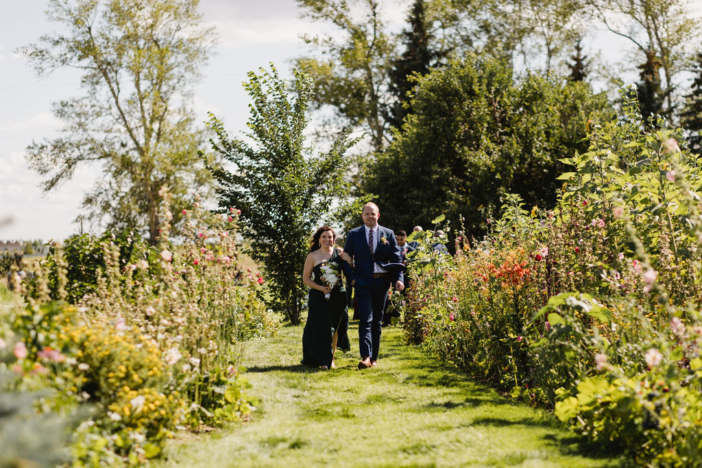 A bride and groom walking through a flower garden.