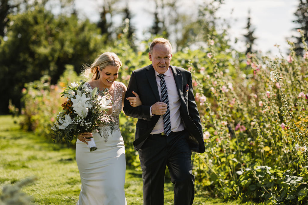 A bride and her father walking through a field of flowers.