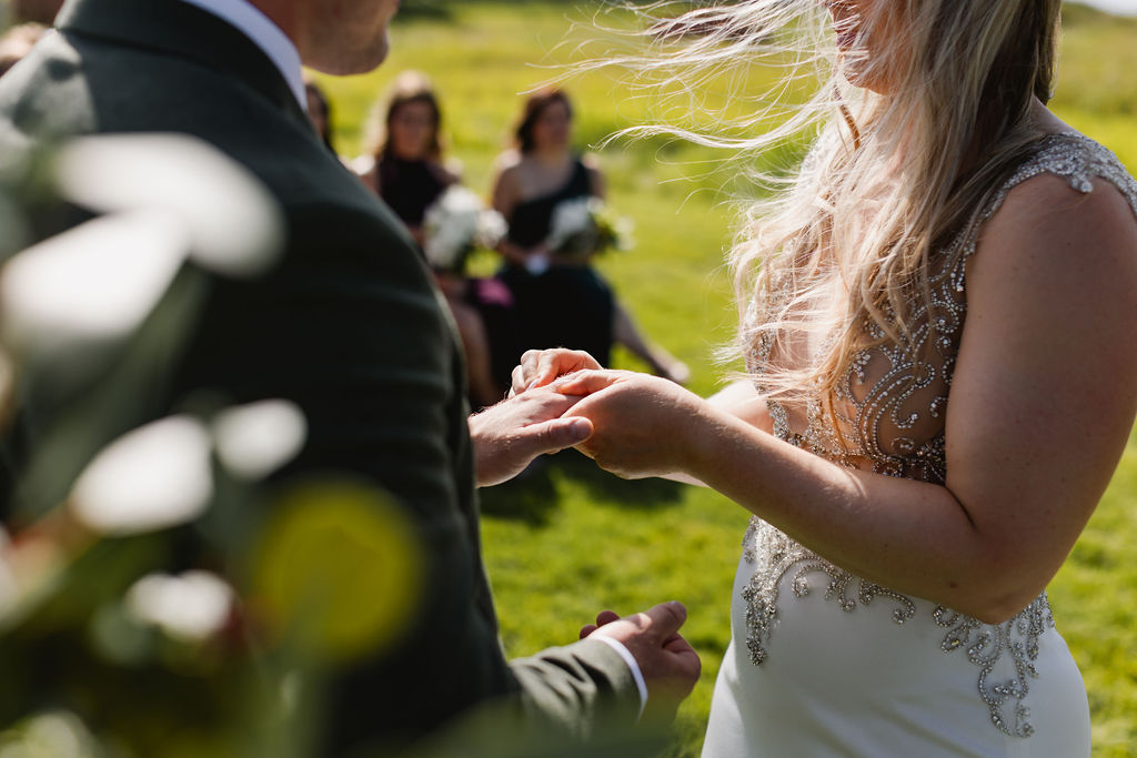 A bride and groom exchanging their wedding rings in a field.
