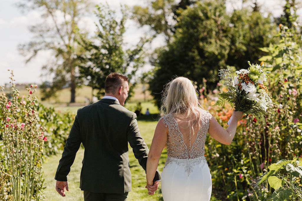 A bride and groom walking through a field of flowers.