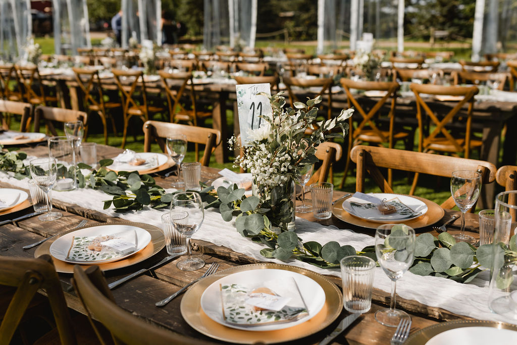 A table set up for a wedding at a farm with gold charger plates, babies breath, diy florlas and greenery.