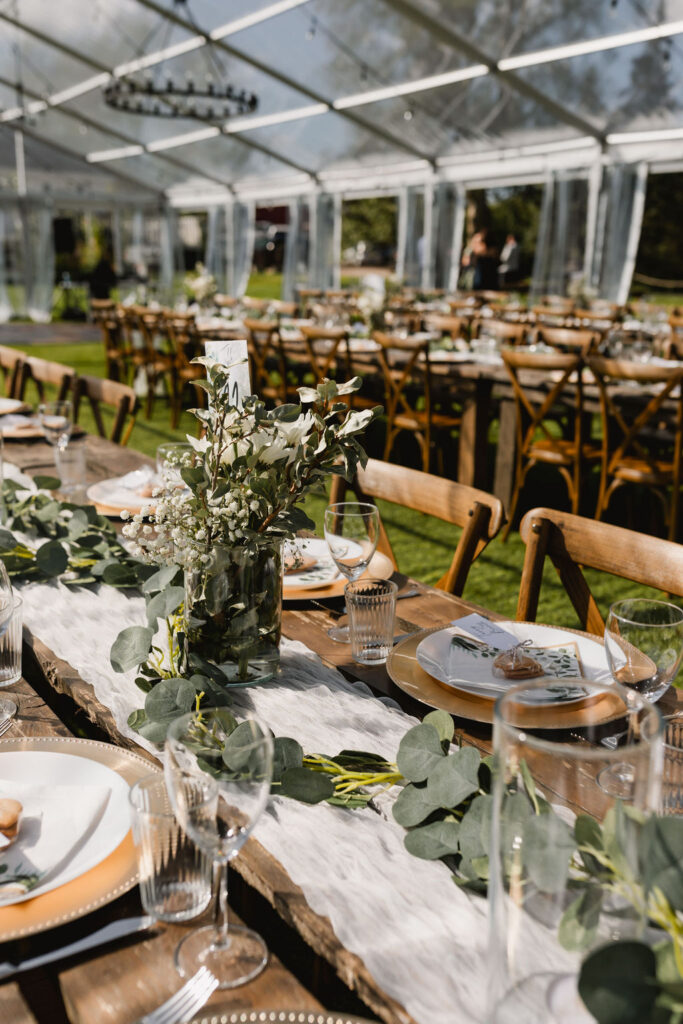 A table set up in a tent with greenery and place settings including diy florals