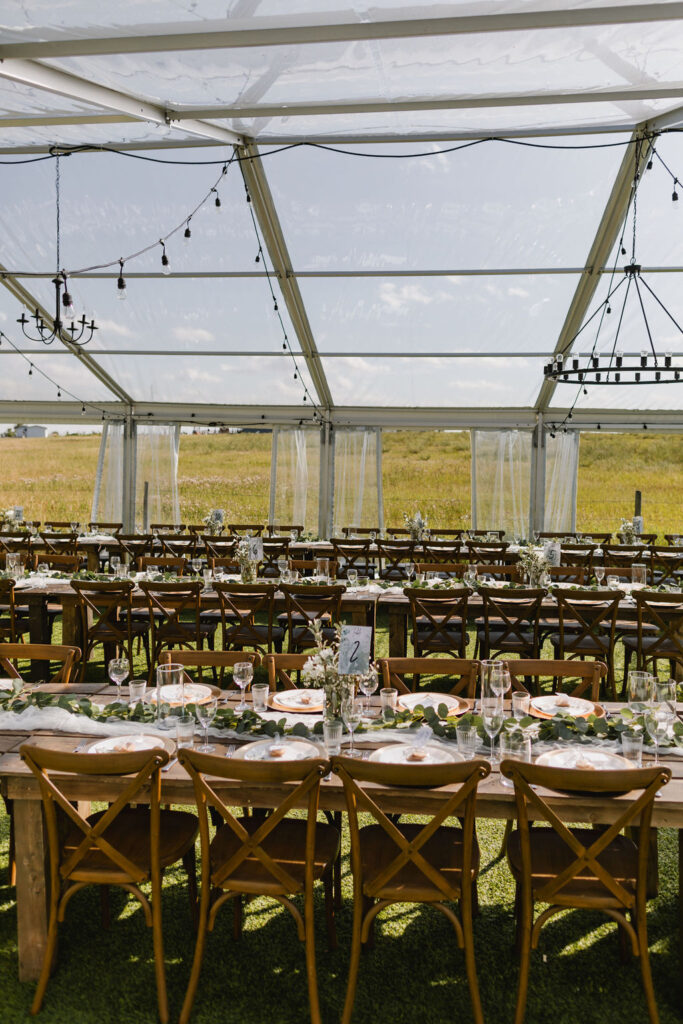 A table set for a wedding reception with wood cross back chairs, harvest tables and diy florals.