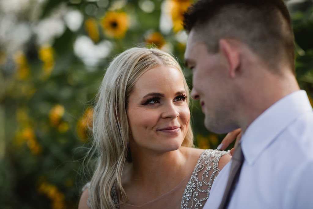 A bride and groom looking at each other in front of sunflowers.