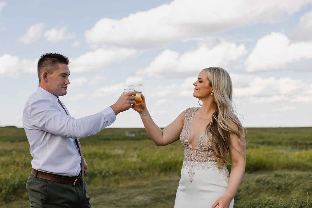 A bride and groom toasting a glass of beer in a field.