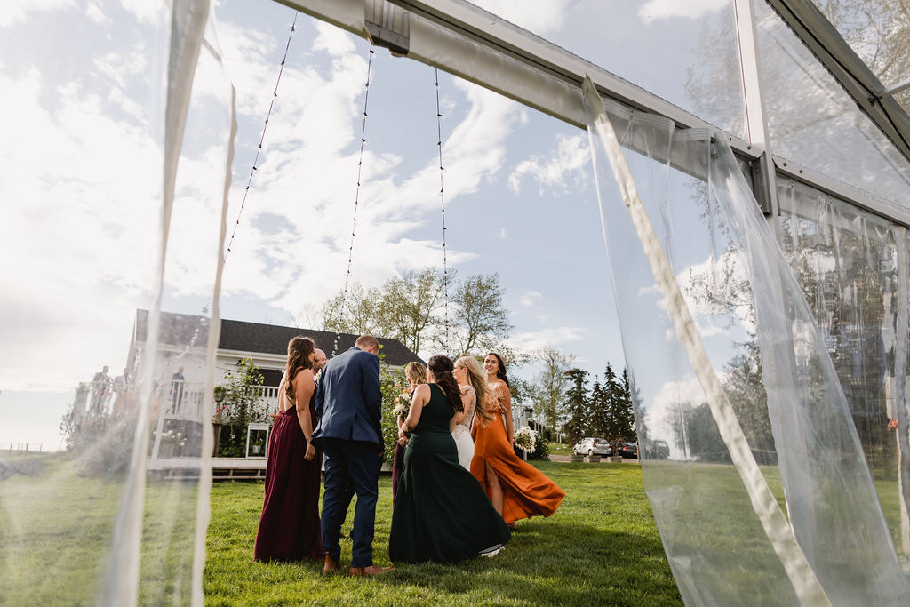 A group of bridesmaids standing in front of a clear tent.