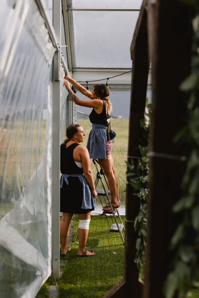 Two women working on the roof of a greenhouse.