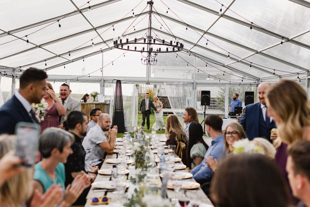 A wedding reception in a tent with people clapping.