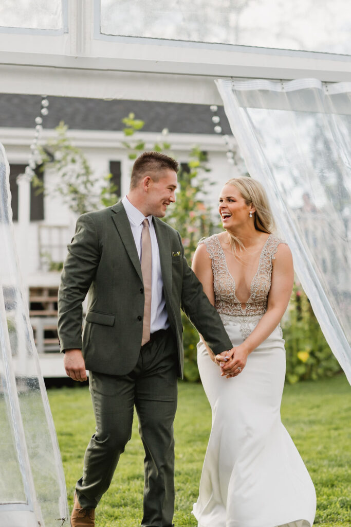 A bride and groom walk through a clear tent at their wedding.