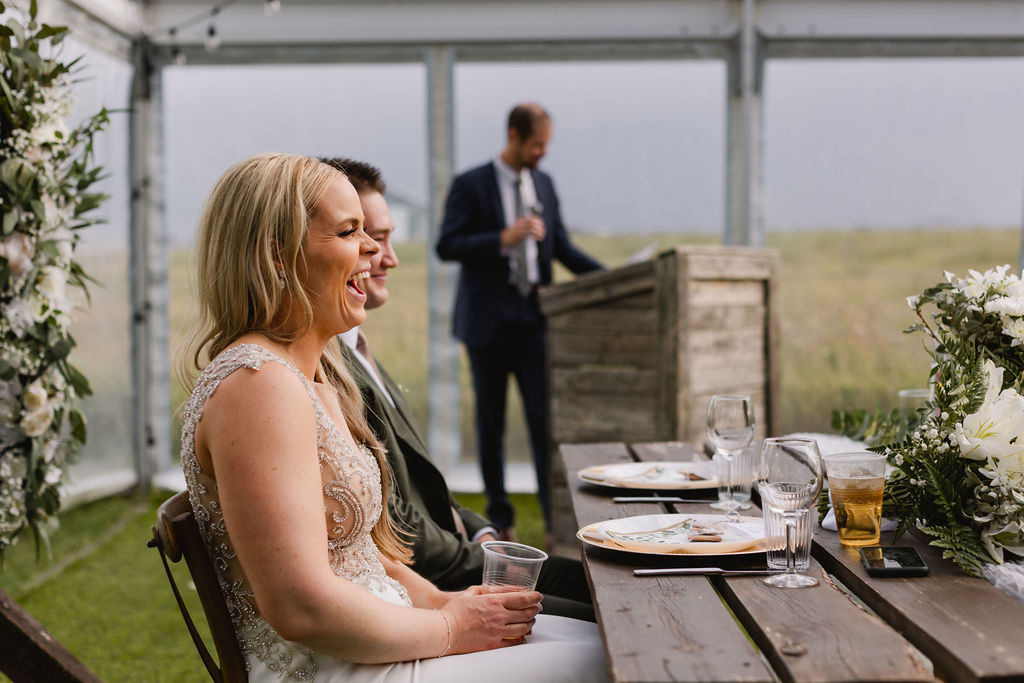 A woman laughing at a table with people in the background.