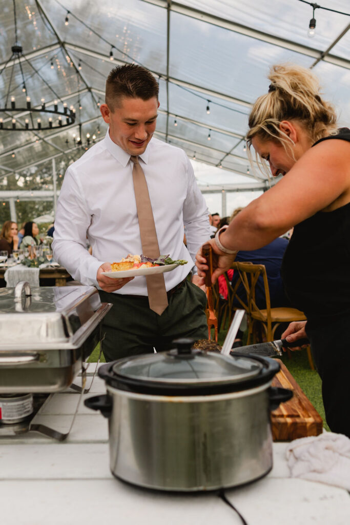 A man and woman serving food in a tent.