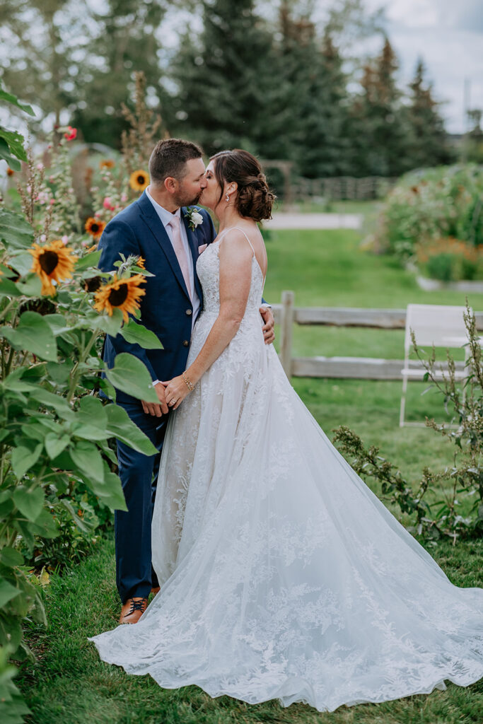 A newlywed couple kissing in an outdoor setting with sunflowers in the background.