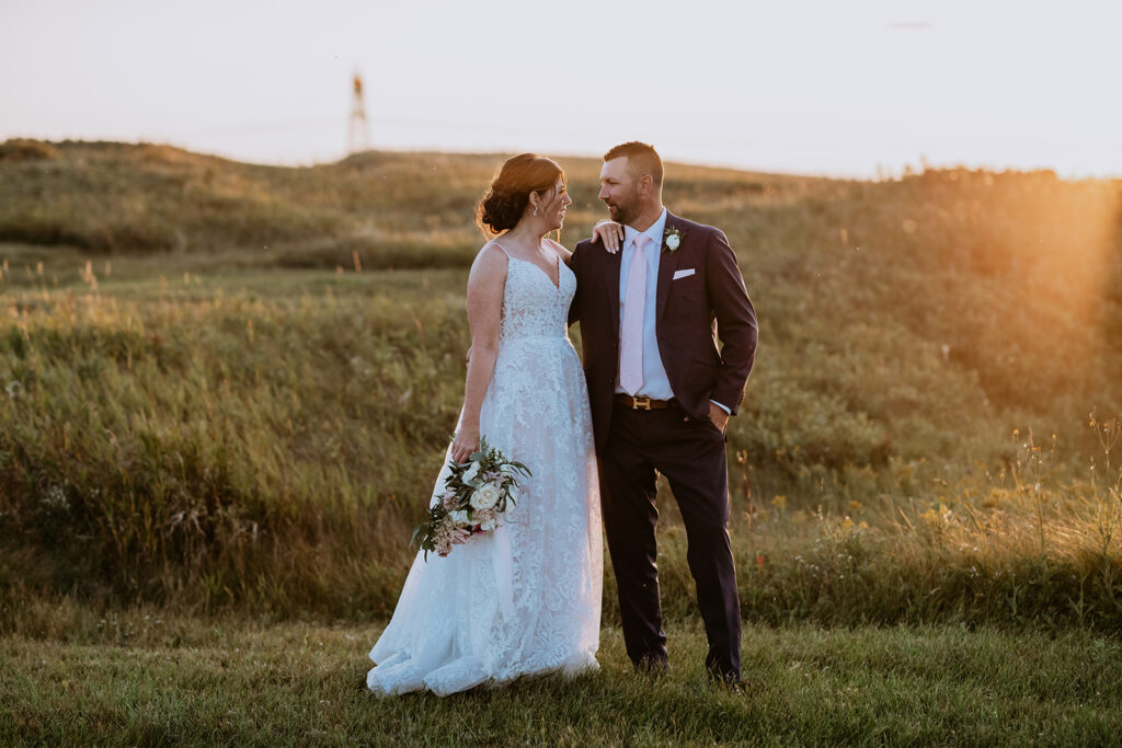 A couple in wedding attire sharing a moment in a field at sunset.