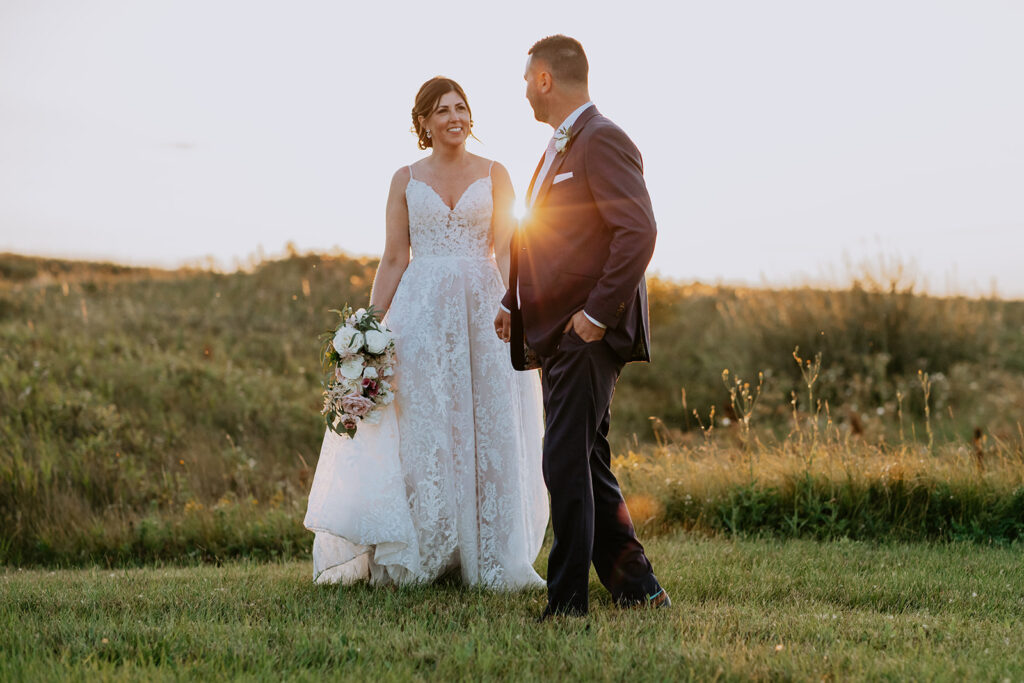 A couple in wedding attire sharing a moment in a field at sunset.