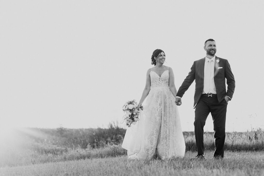 Bride and groom holding hands and smiling in a field.